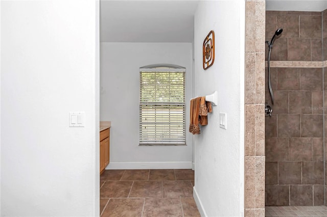 full bathroom featuring tile patterned flooring, baseboards, a tile shower, and vanity