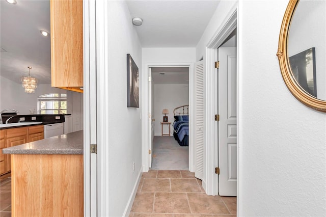 hallway with a notable chandelier, baseboards, a sink, and light tile patterned flooring