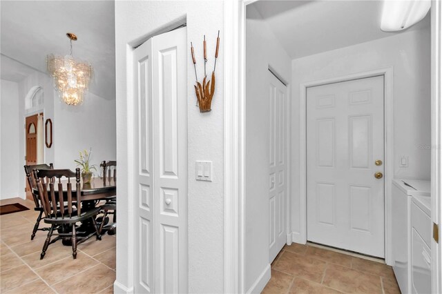 hallway featuring separate washer and dryer, light tile patterned floors, and an inviting chandelier