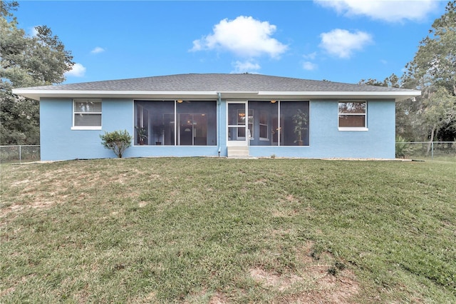 back of house featuring a sunroom, stucco siding, fence, and a lawn