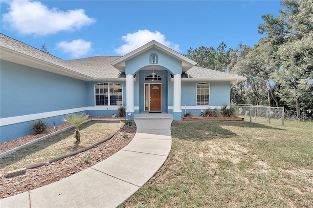 view of front of house with roof with shingles, fence, a front lawn, and stucco siding