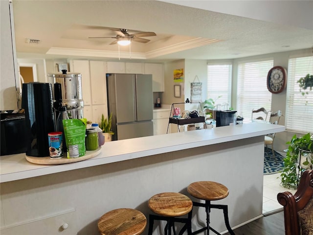 kitchen featuring hardwood / wood-style floors, a tray ceiling, kitchen peninsula, stainless steel refrigerator, and ceiling fan