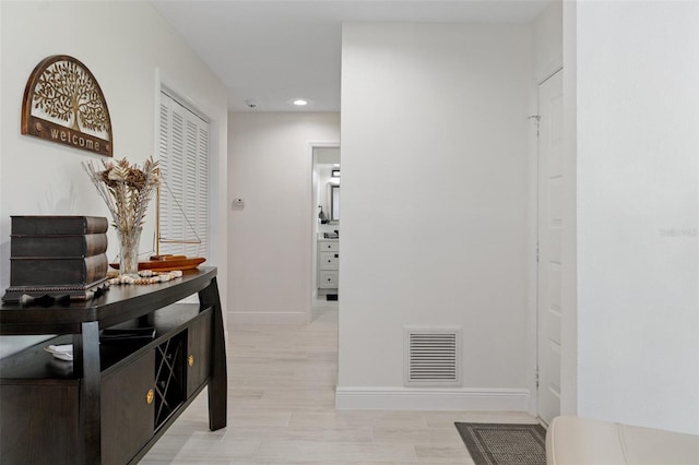 hallway featuring light wood-type flooring, baseboards, visible vents, and recessed lighting