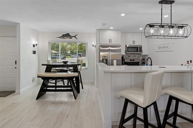 kitchen with stainless steel appliances, tasteful backsplash, visible vents, light wood-style floors, and a kitchen breakfast bar