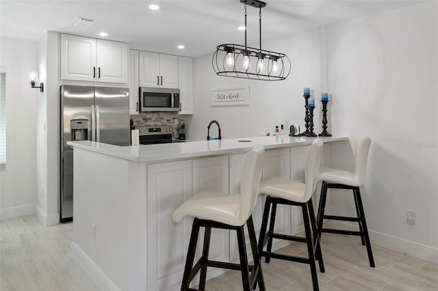 kitchen featuring appliances with stainless steel finishes, light hardwood / wood-style flooring, tasteful backsplash, white cabinets, and hanging light fixtures