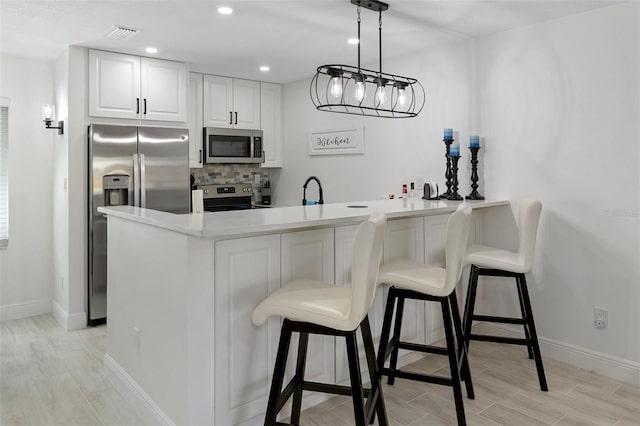 kitchen with visible vents, a breakfast bar area, appliances with stainless steel finishes, a peninsula, and backsplash