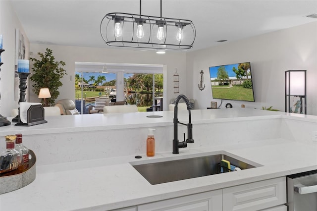 kitchen with hanging light fixtures, dishwashing machine, white cabinetry, light stone countertops, and sink