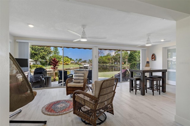 living room with a wealth of natural light, ceiling fan, light hardwood / wood-style floors, and a textured ceiling