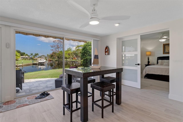 dining room with ceiling fan, a textured ceiling, and a water view