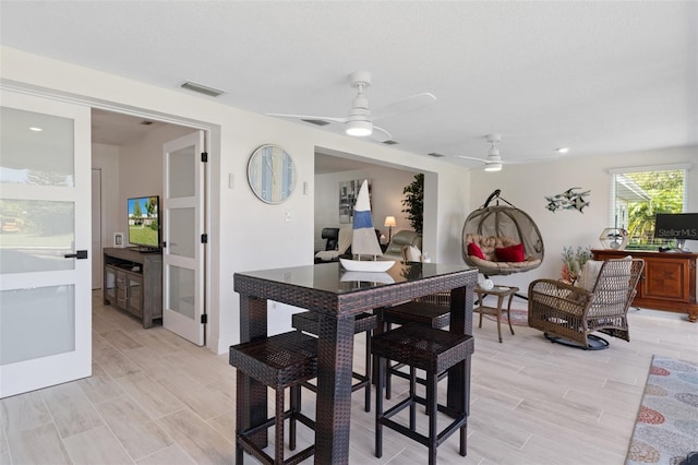 dining space with a textured ceiling, wood finish floors, visible vents, and a ceiling fan