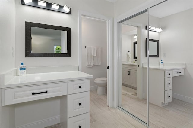 full bathroom with wood finish floors, baseboards, two vanities, and toilet