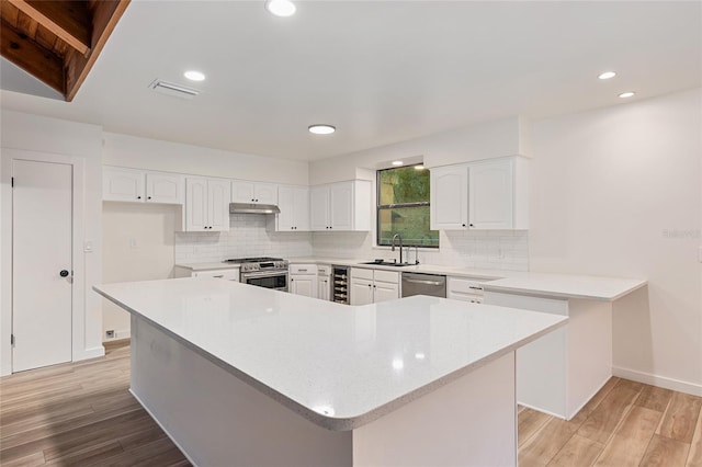 kitchen with appliances with stainless steel finishes, decorative backsplash, white cabinets, and light wood-type flooring