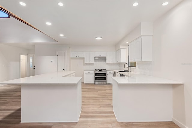 kitchen with light hardwood / wood-style flooring, decorative backsplash, sink, range with two ovens, and white cabinets