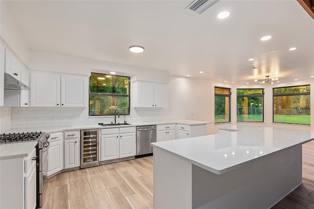 kitchen with appliances with stainless steel finishes, light hardwood / wood-style floors, white cabinets, and beverage cooler