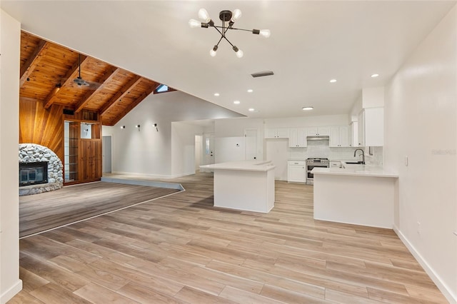 kitchen with vaulted ceiling with beams, light wood-type flooring, wooden ceiling, a fireplace, and stainless steel range