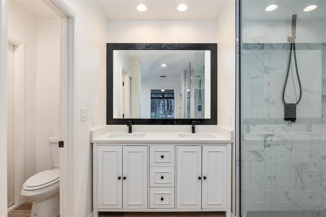 bathroom with a shower with shower door, toilet, double sink vanity, and wood-type flooring