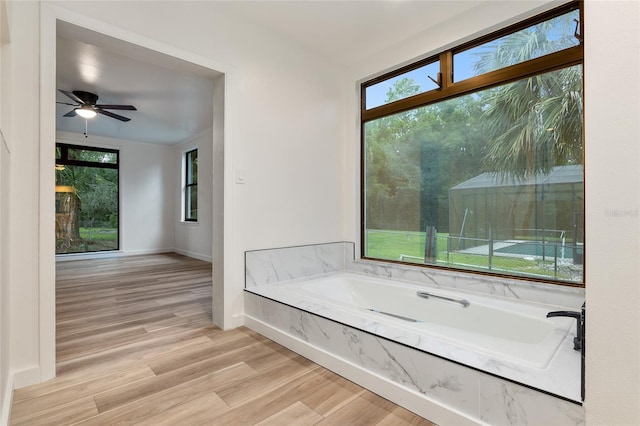 interior space with tiled tub, hardwood / wood-style flooring, and ceiling fan