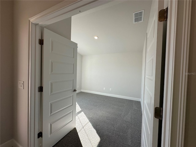 empty room with vaulted ceiling, dark carpet, visible vents, and baseboards