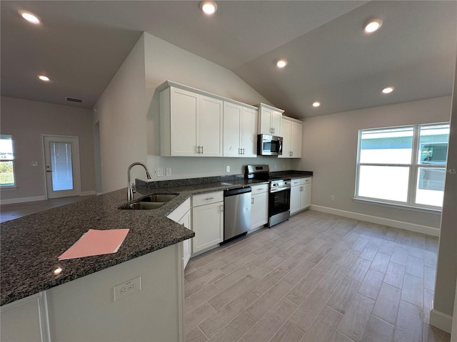 kitchen with a sink, white cabinets, vaulted ceiling, appliances with stainless steel finishes, and dark stone countertops