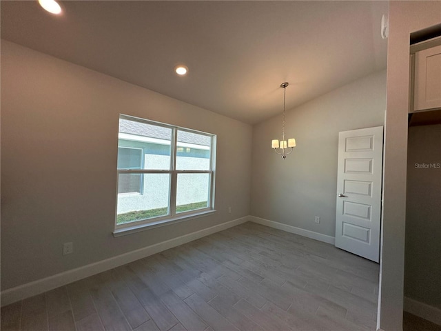 spare room with a notable chandelier, recessed lighting, vaulted ceiling, wood finished floors, and baseboards