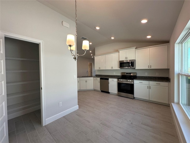 kitchen featuring dark countertops, appliances with stainless steel finishes, white cabinets, vaulted ceiling, and a sink