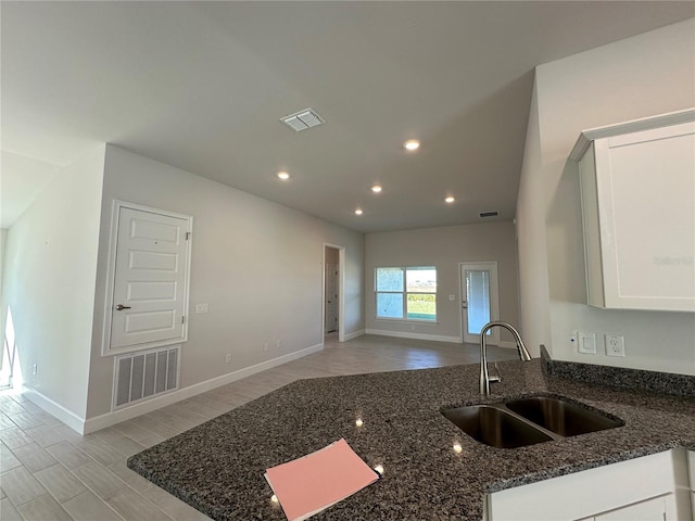 kitchen with white cabinetry, dark stone countertops, visible vents, and a sink