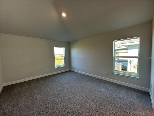 empty room featuring vaulted ceiling, dark colored carpet, and baseboards