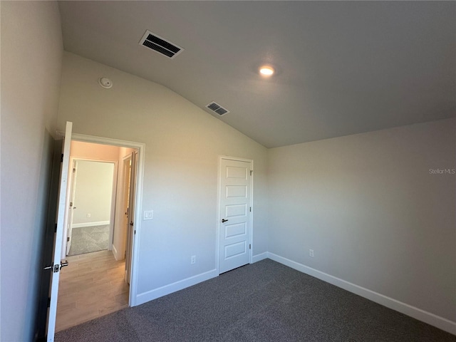 empty room with lofted ceiling, dark carpet, visible vents, and baseboards