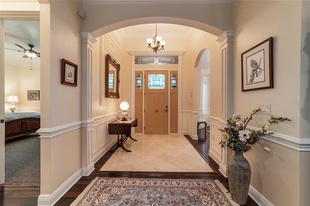 entrance foyer featuring crown molding, ceiling fan with notable chandelier, hardwood / wood-style floors, and ornate columns