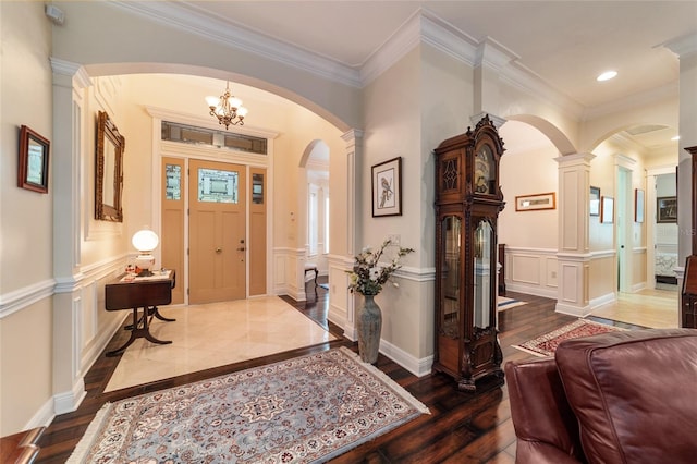 foyer with an inviting chandelier, hardwood / wood-style floors, ornamental molding, and decorative columns