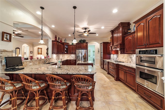 kitchen with appliances with stainless steel finishes, kitchen peninsula, ceiling fan, a breakfast bar, and hanging light fixtures