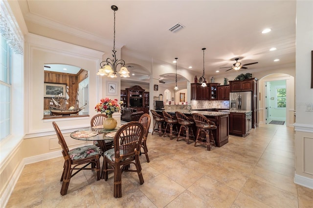 dining space with ceiling fan with notable chandelier, crown molding, and light tile patterned flooring