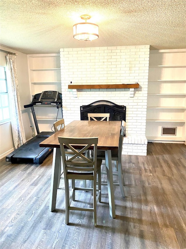 dining area featuring a textured ceiling, hardwood / wood-style floors, and a brick fireplace