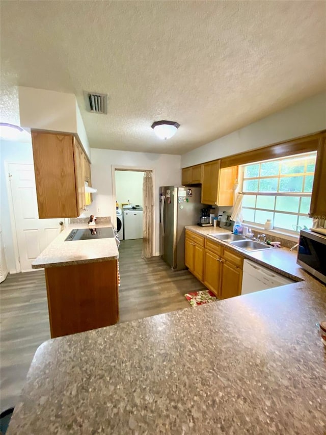 kitchen with sink, separate washer and dryer, kitchen peninsula, hardwood / wood-style flooring, and stainless steel appliances