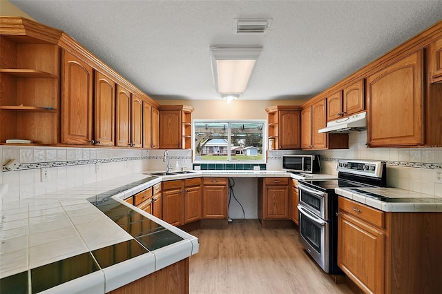 kitchen featuring tile counters, under cabinet range hood, appliances with stainless steel finishes, and open shelves