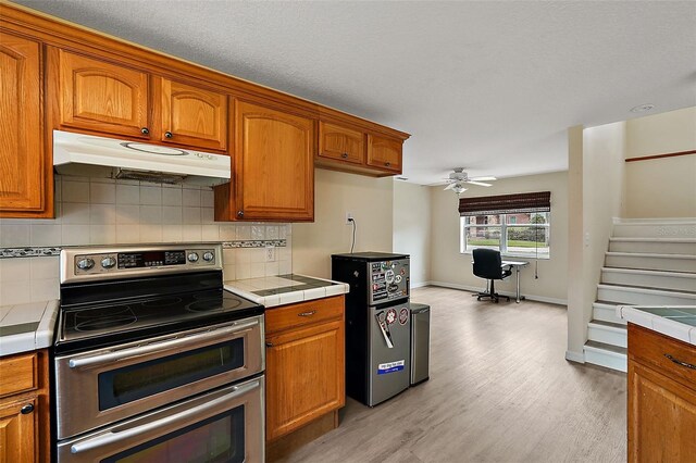 kitchen featuring stainless steel electric stove, light wood-type flooring, tasteful backsplash, tile countertops, and ceiling fan