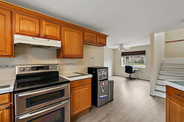 kitchen featuring tile countertops, range with two ovens, decorative backsplash, and under cabinet range hood