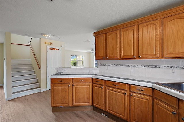 kitchen with decorative backsplash, tile counters, light hardwood / wood-style floors, kitchen peninsula, and a textured ceiling