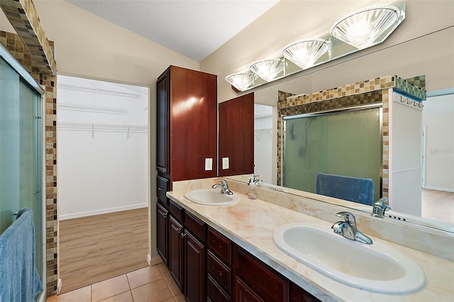 bathroom with dual vanity, vaulted ceiling, hardwood / wood-style floors, and a shower with shower door