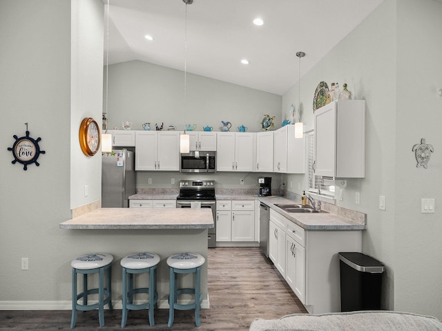 kitchen featuring vaulted ceiling, light wood-type flooring, stainless steel appliances, white cabinetry, and a breakfast bar area