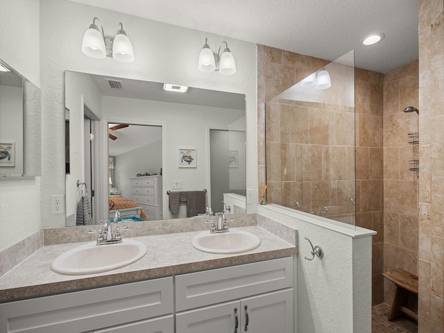 bathroom with tiled shower, ceiling fan, a textured ceiling, and vanity