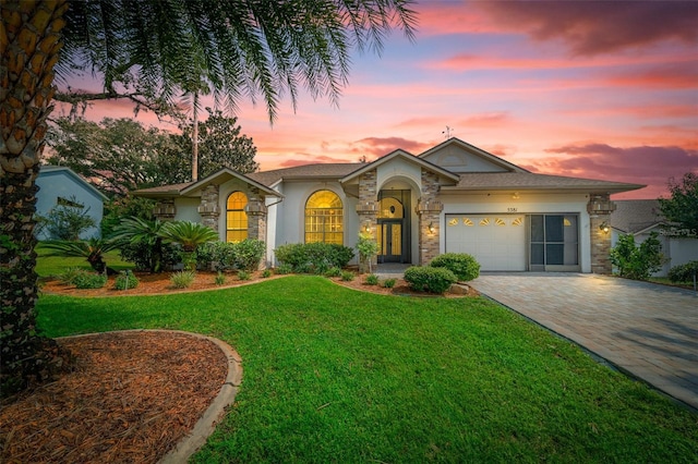 view of front of property with a garage, a yard, stone siding, decorative driveway, and stucco siding