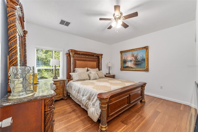 bedroom with a ceiling fan, wood finished floors, visible vents, and baseboards