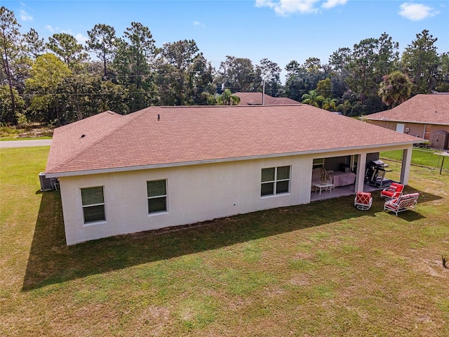 rear view of property featuring a yard, a shingled roof, a patio area, and stucco siding