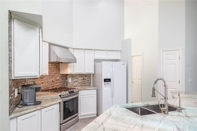 kitchen featuring white cabinets, wall chimney exhaust hood, white fridge with ice dispenser, and stainless steel range oven