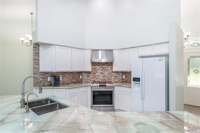 kitchen with a notable chandelier, white fridge with ice dispenser, stainless steel range, hanging light fixtures, and wall chimney exhaust hood