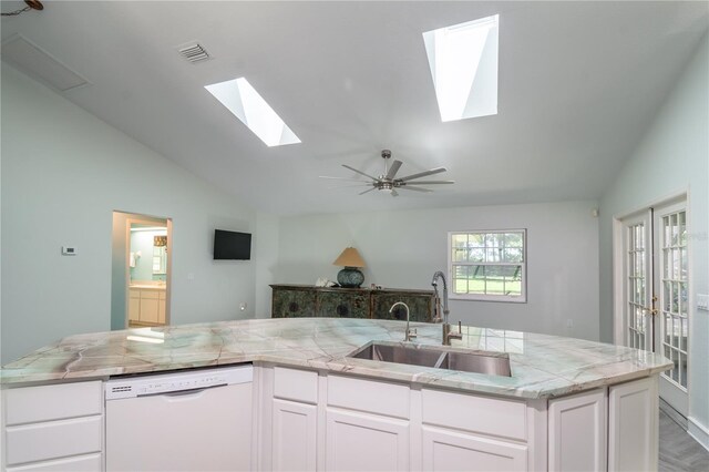 kitchen featuring vaulted ceiling with skylight, white cabinetry, dishwasher, sink, and ceiling fan