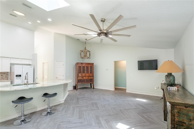 interior space with a skylight, baseboards, visible vents, a ceiling fan, and high vaulted ceiling