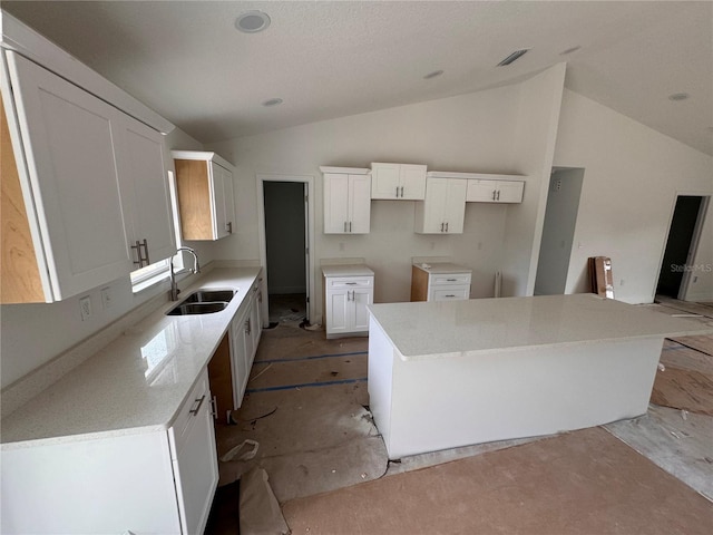 kitchen featuring sink, light stone countertops, a kitchen island, white cabinetry, and lofted ceiling