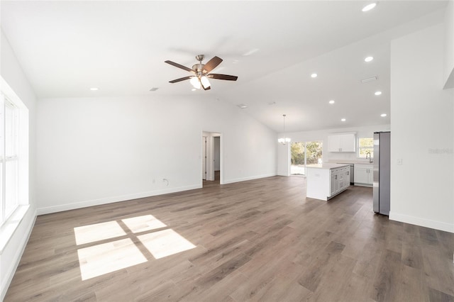 unfurnished living room with ceiling fan with notable chandelier, lofted ceiling, sink, and hardwood / wood-style floors